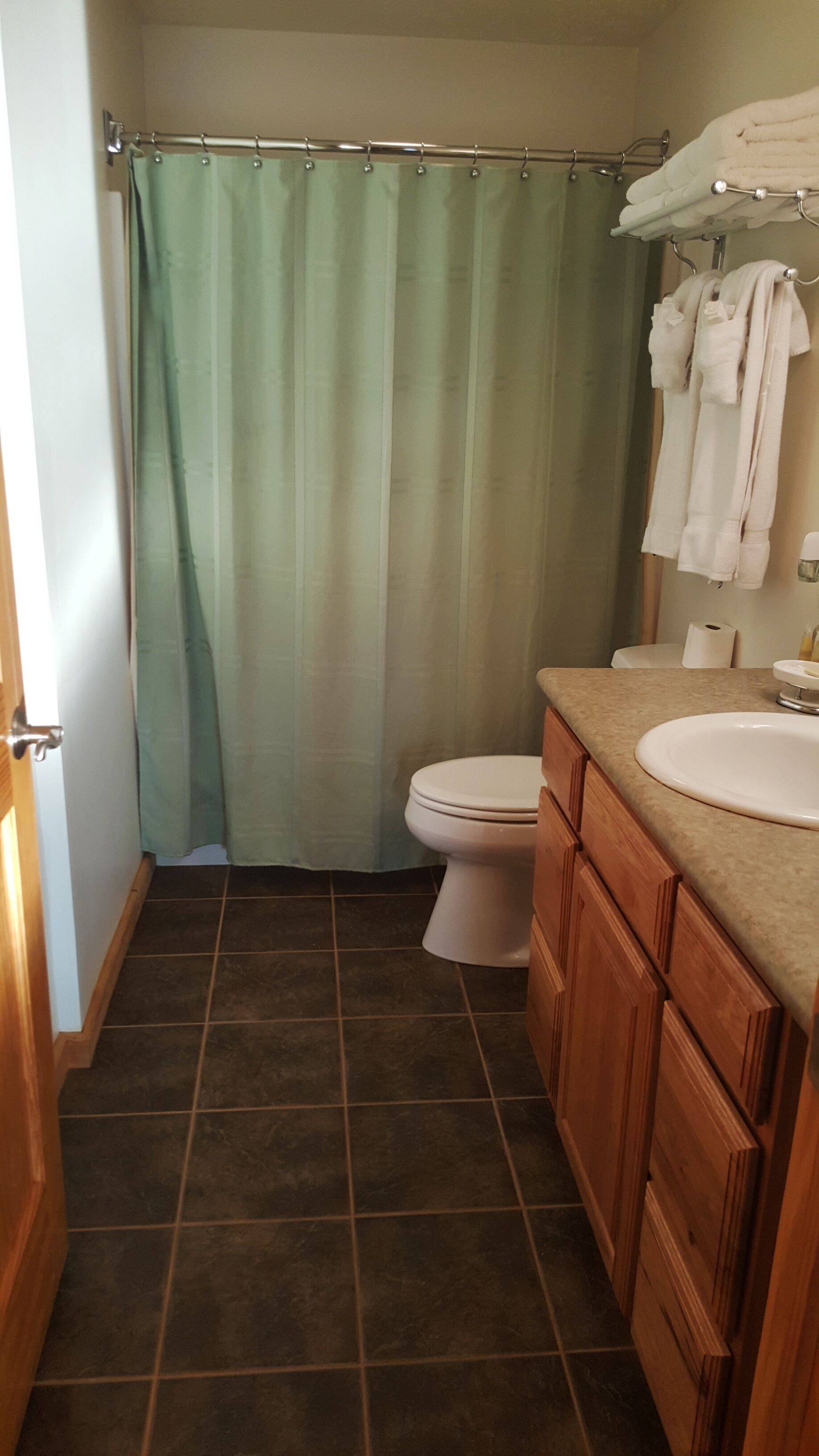 A bathroom with a shower curtain, toilet, sink, and wooden cabinets.