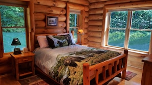 A log cabin bedroom with a bed, a nightstand, a lamp, and a picture on the wall. - Family-friendly log home between Harbor Springs, Petoskey, and Mackinaw Island (Pellston)