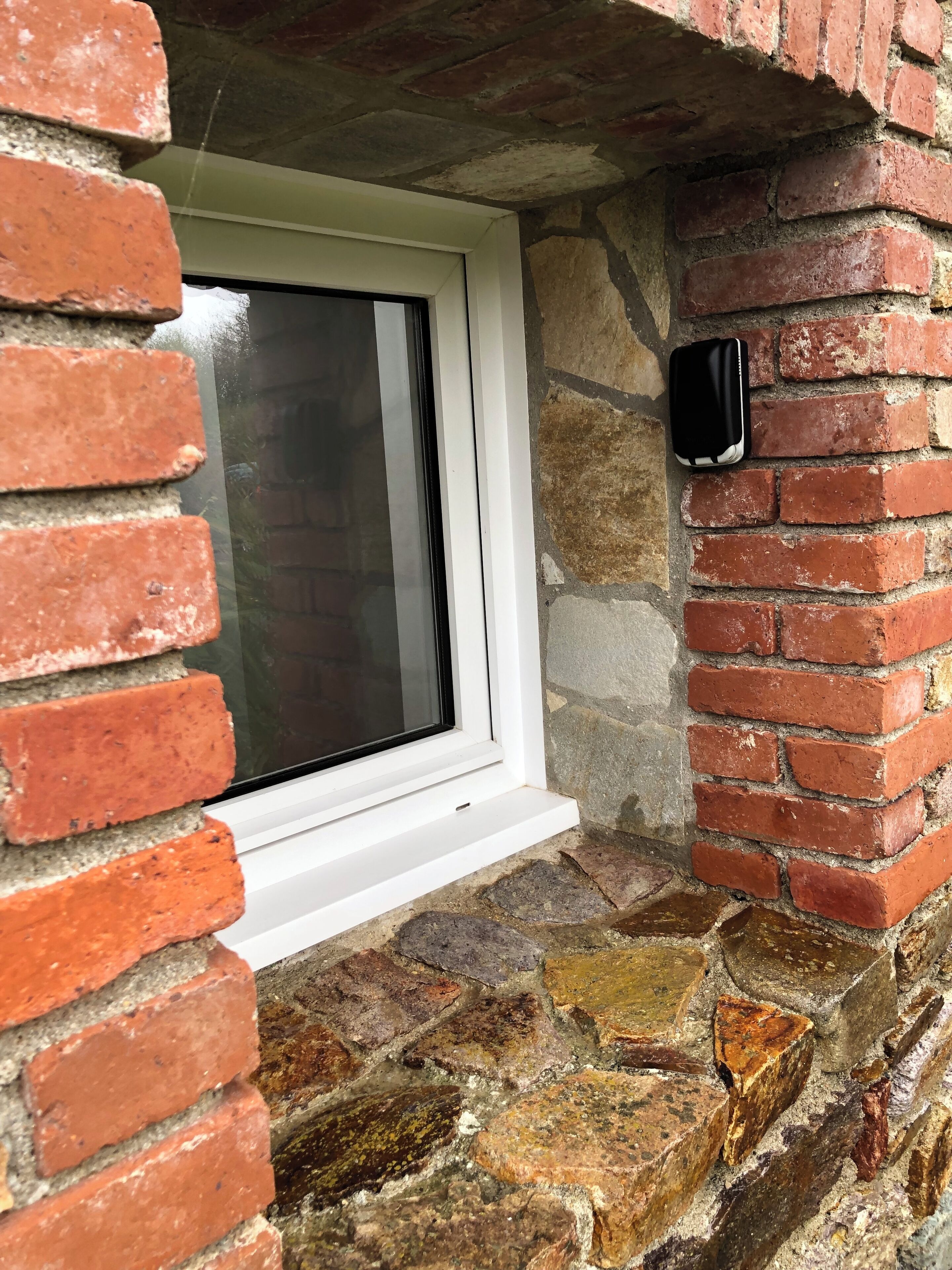 A window with a white frame, set in a stone wall with red bricks.