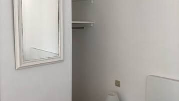 Un dormitorio con cama, mesita de noche con lámpara, armario blanco y espejo en la pared.