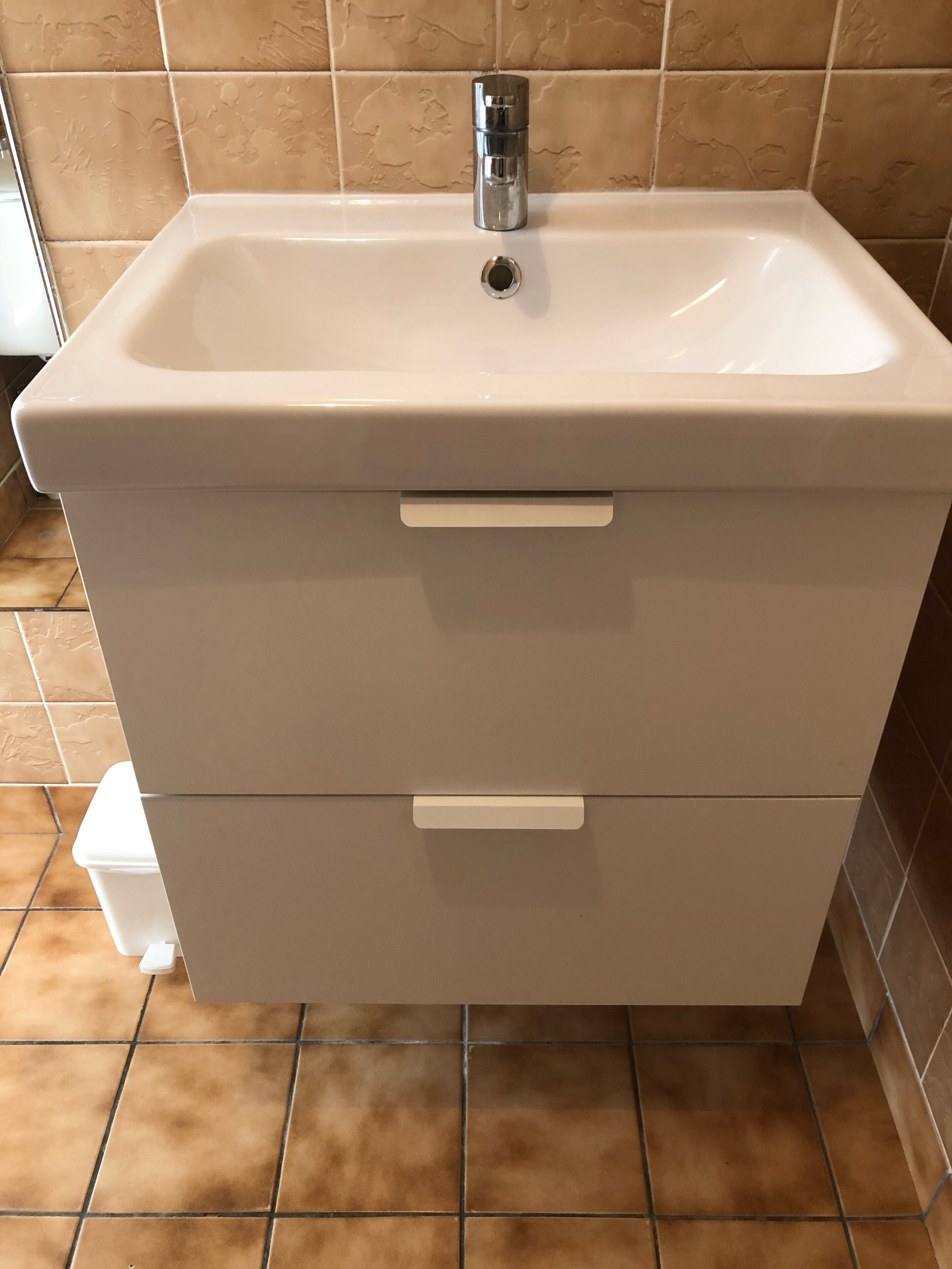 Ein Badezimmer mit einem weißen Waschbecken, zwei Schubladen und einem chromfarbenen Wasserhahn.