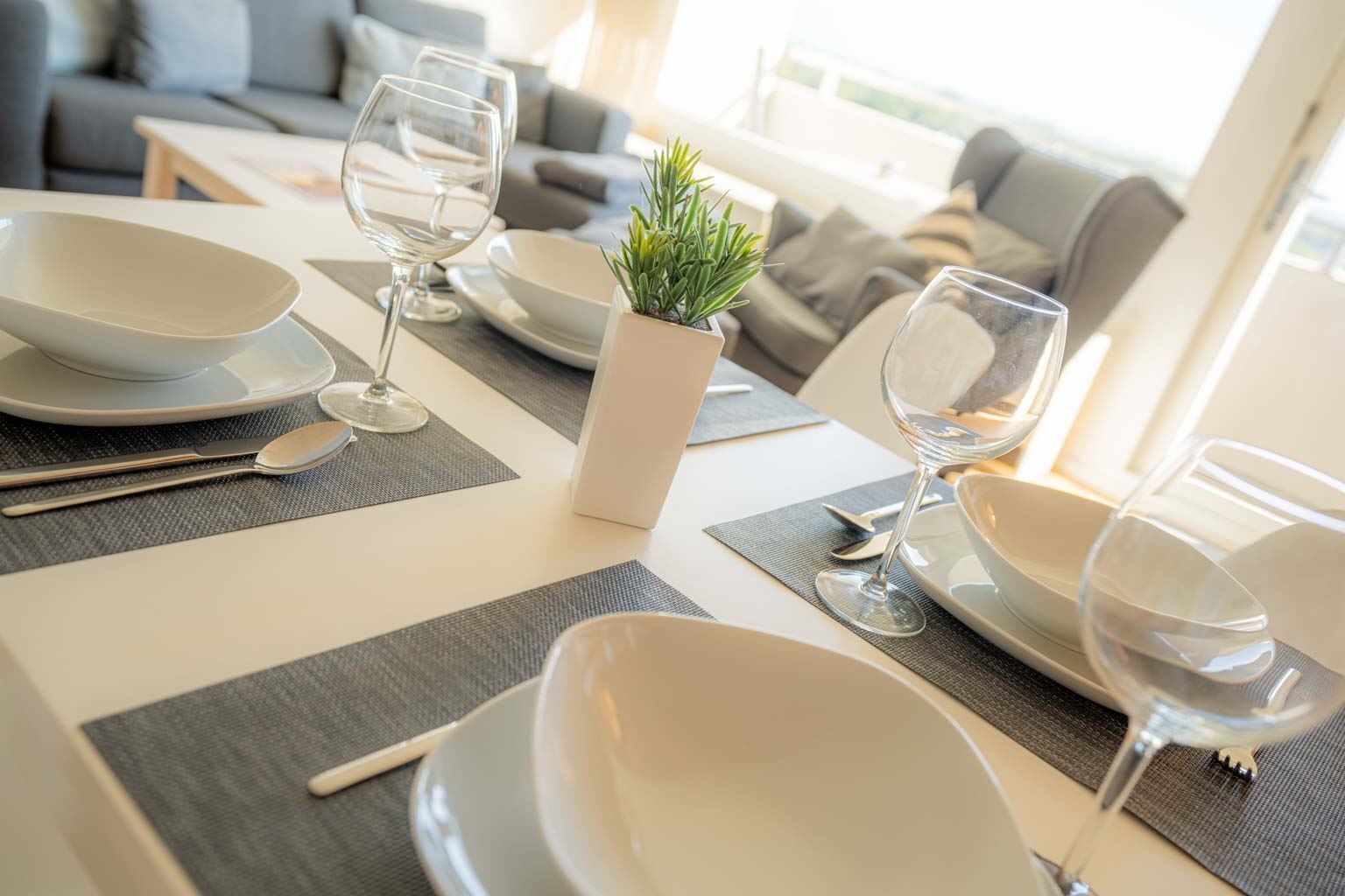 A dining area with a table set for four, including plates, bowls, cutlery, and wine glasses.