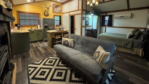 Interior acogedor de una cabaña con techo de madera, chimenea, zona de cocina, sofá y cama.