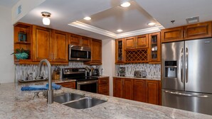 Una cocina con armarios de madera, electrodomésticos de acero inoxidable, encimera de granito y un lavamanos doble.