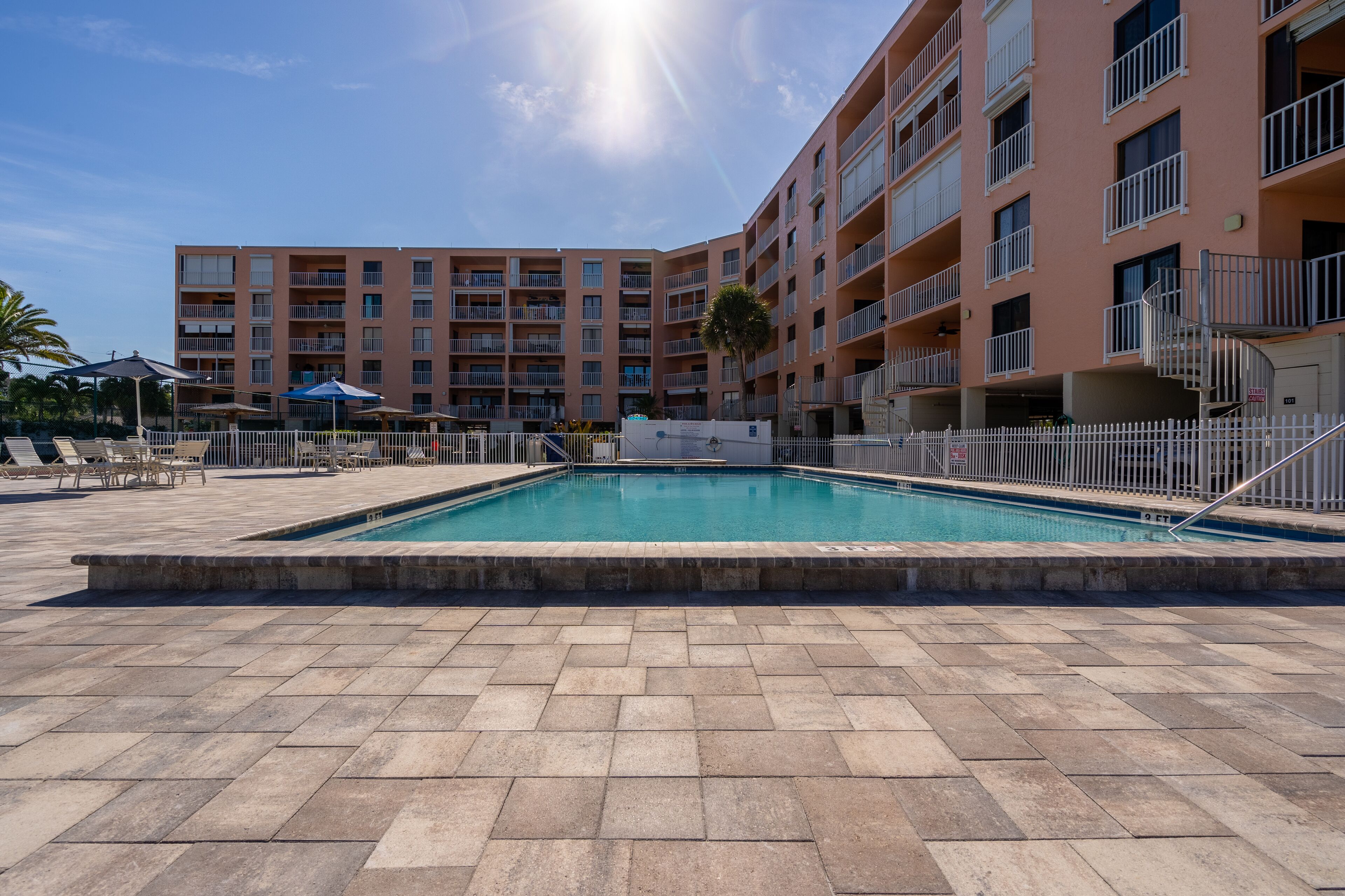 Una piscina circondata da un recinto bianco, con un edificio a più piani sullo sfondo.