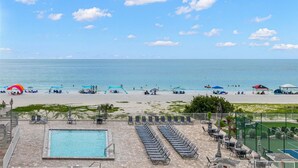 Una playa con piscina, sillas de descanso y sombrillas.