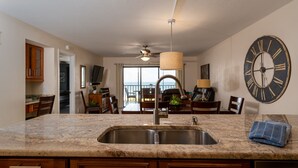 Una cocina con encimeras de granito, pileta de acero inoxidable, muebles de madera y un reloj de pared grande.