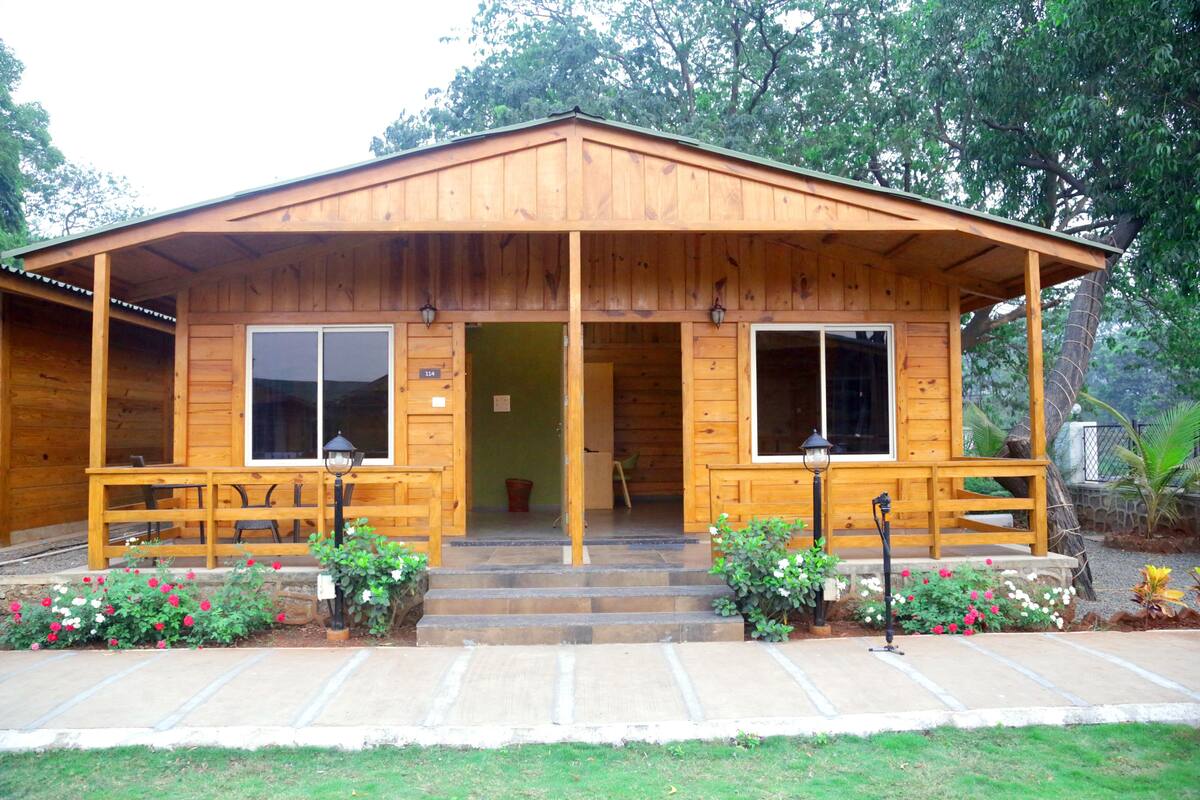 A wooden cabin with a porch, large windows, and a stone pathway leading to the entrance.