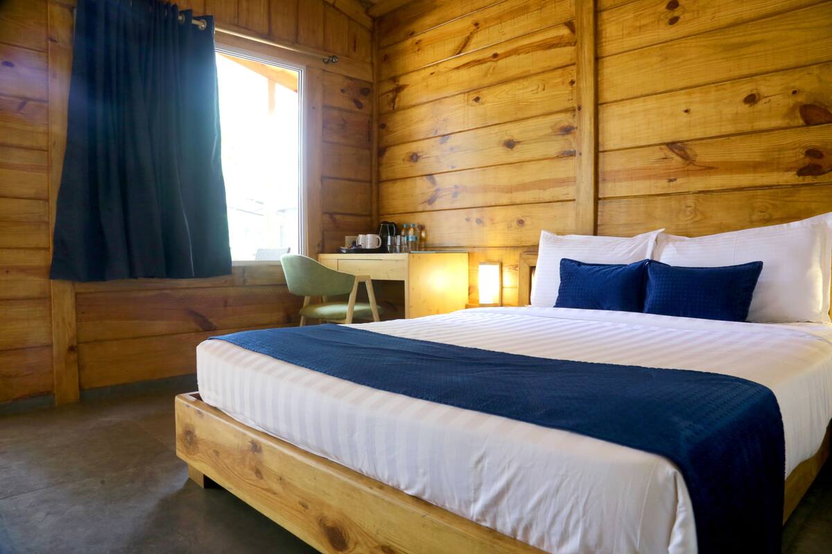 A wooden cabin room with a bed, a desk, and a chair.