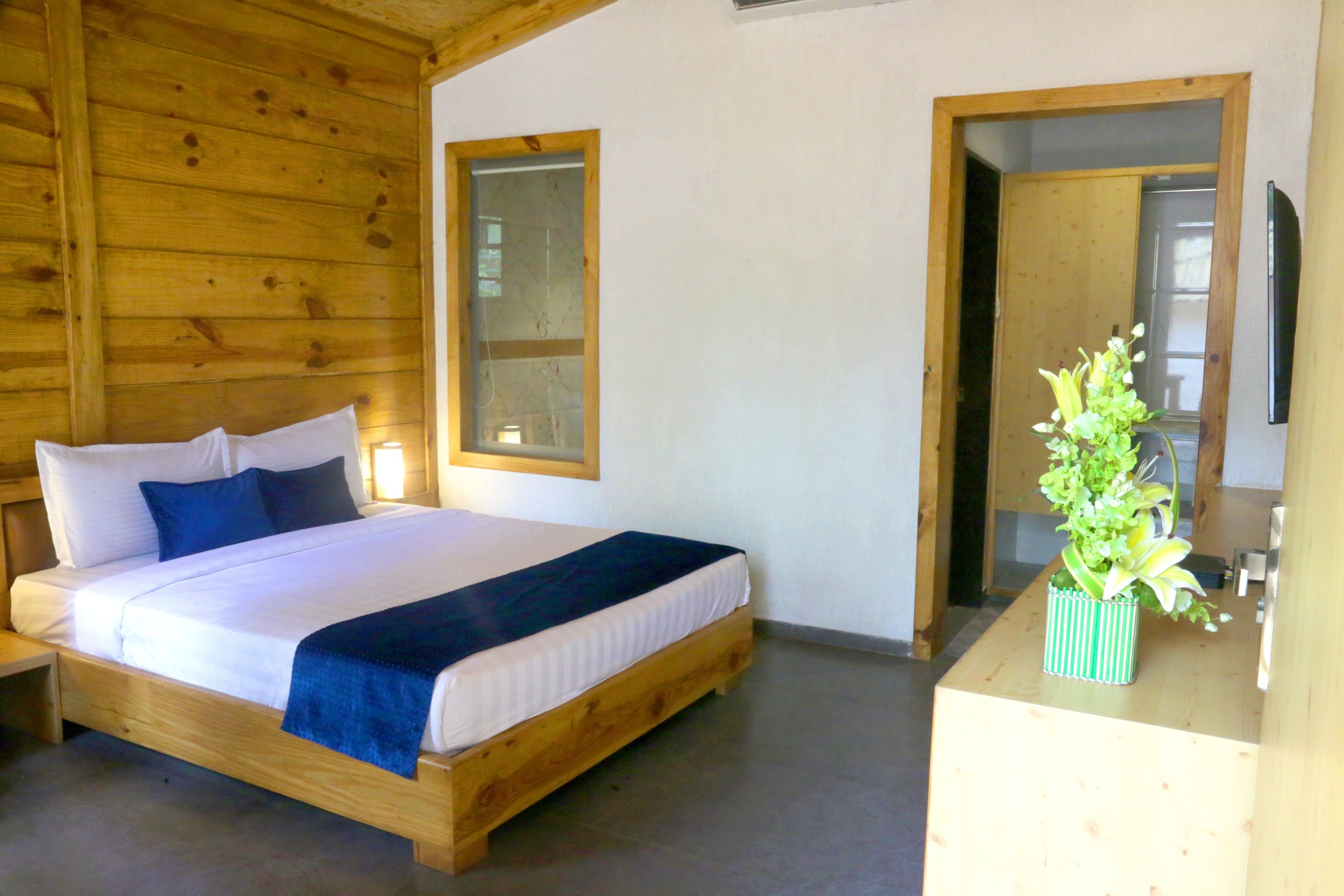 Una cama con estructura de madera, ropa de cama blanca y detalles azules, una mesita de noche y una lámpara pequeña junto a la cama.