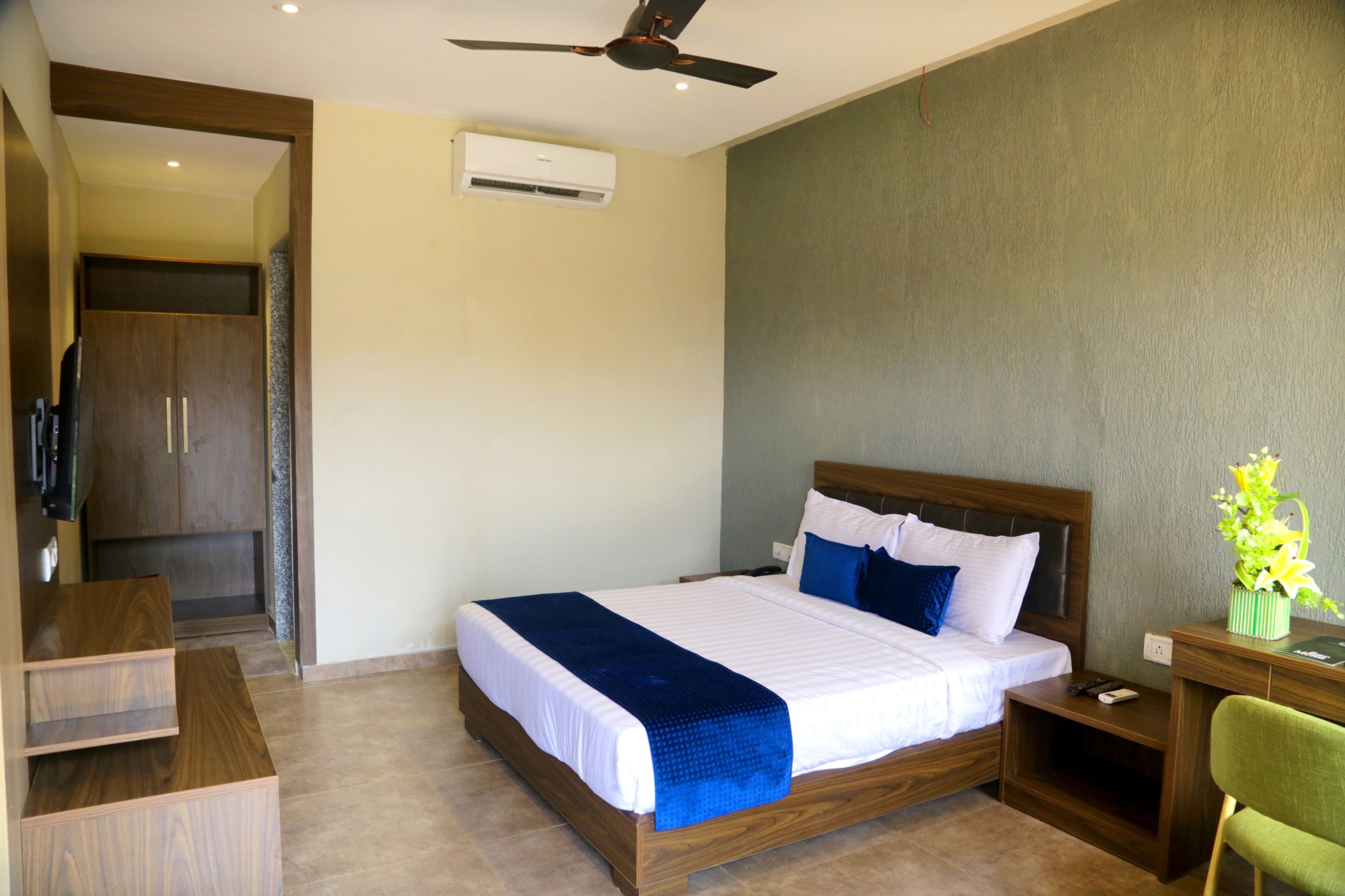 Habitación de hotel con cama, escritorio, silla, ventilador de techo y aire acondicionado.