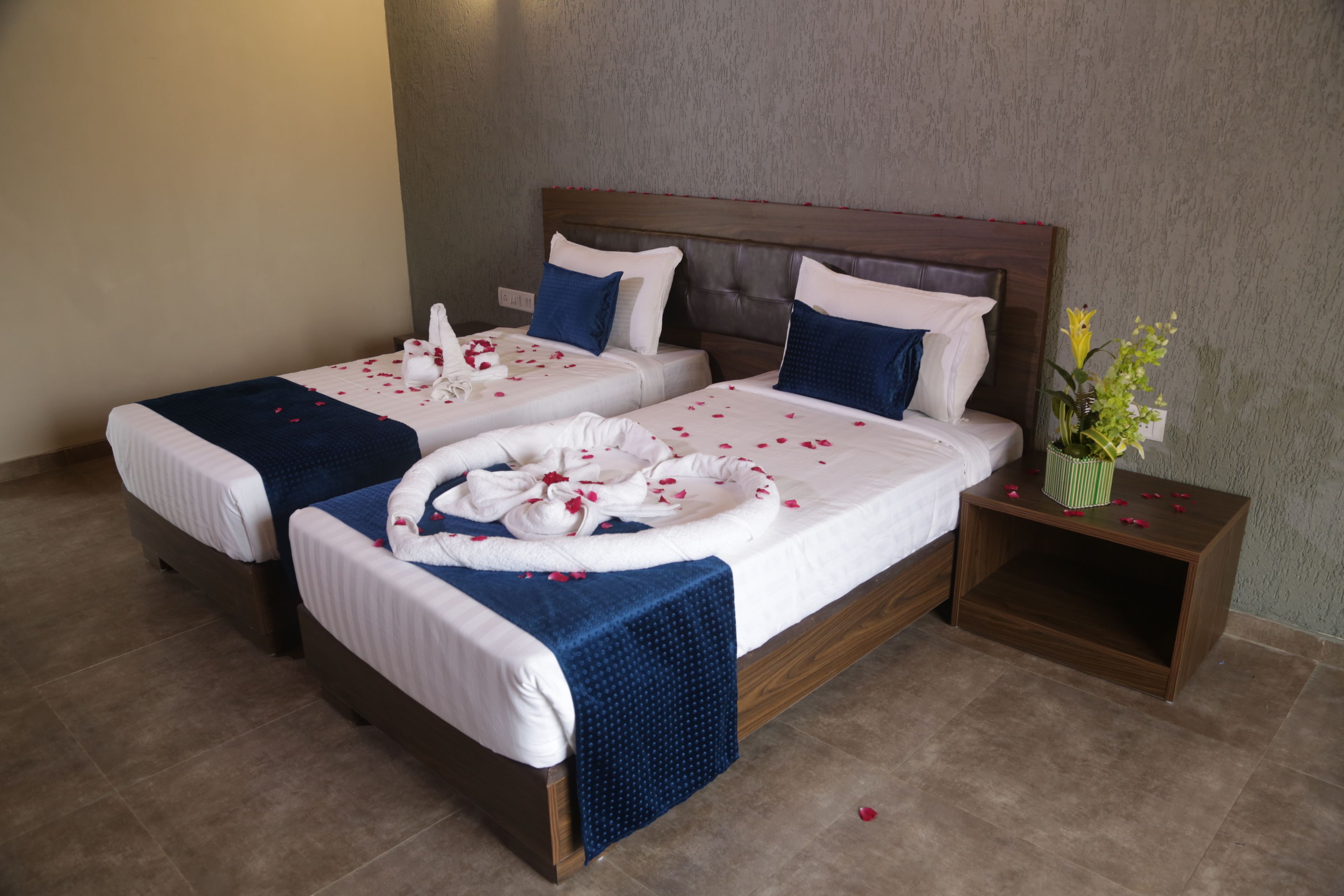 A hotel room with two beds, a wooden headboard, and a small bedside table with a vase of flowers.