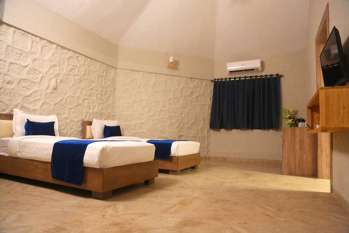 A bedroom with two beds, a stone wall, a TV, and an air conditioning unit.