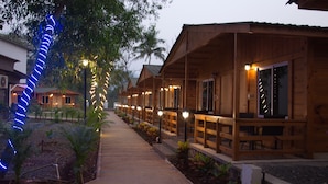 A row of wooden cabins with outdoor seating and string lights. - Sai River Resort (Khalapur)