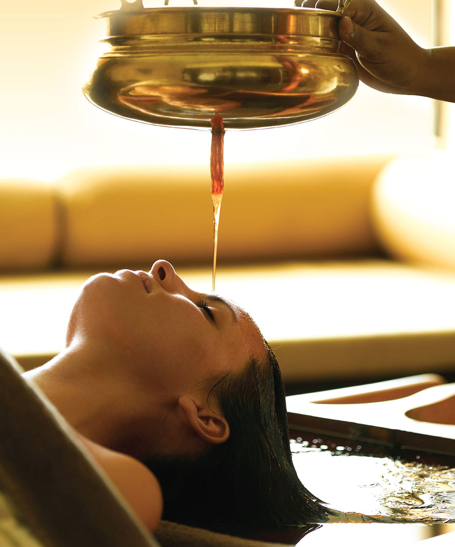 A person receiving a treatment with a liquid being poured from a metallic container.