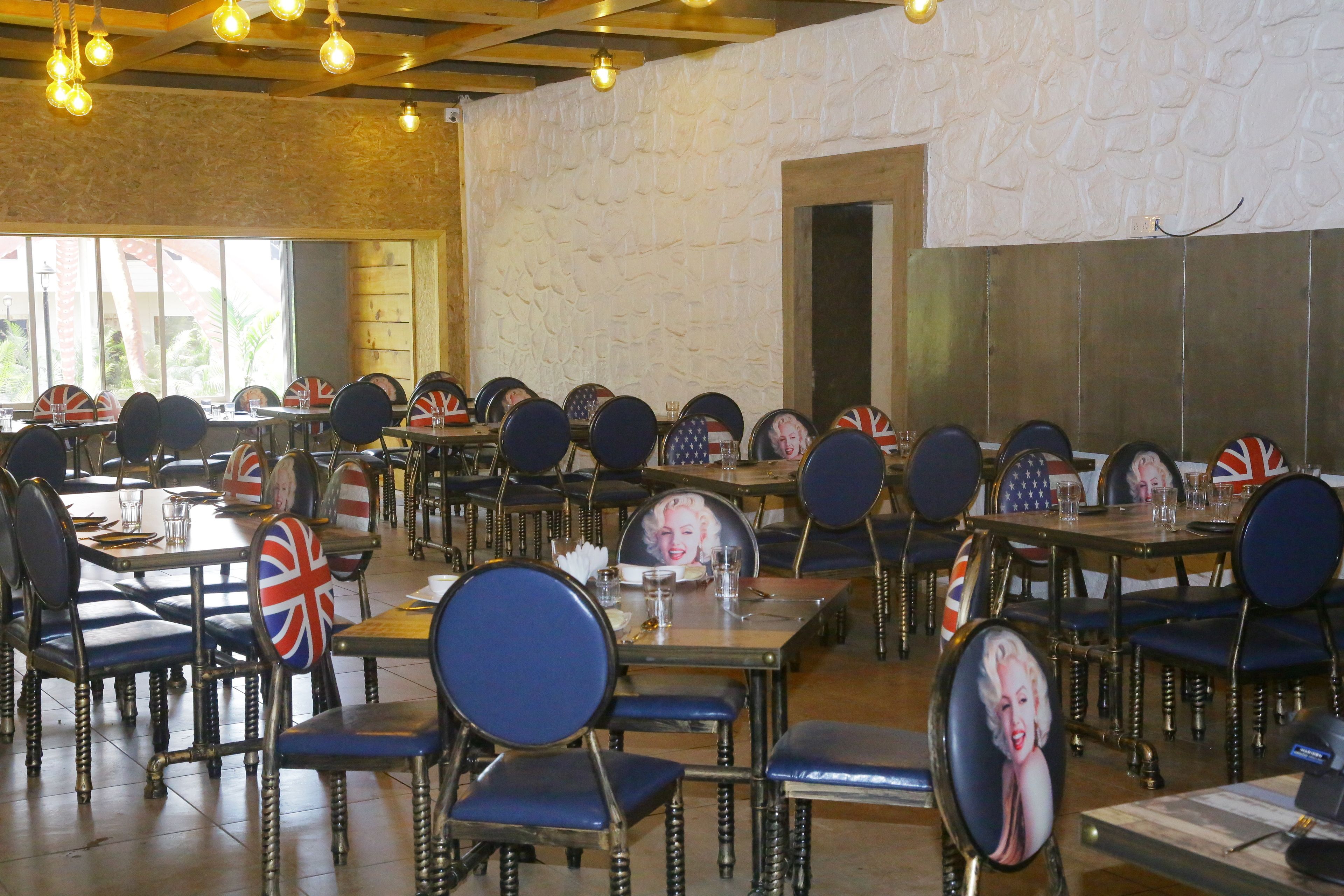 Un restaurante con varias mesas y sillas, cada una con una bandera Union Jack. La sala tiene techo de madera rústica y paredes de piedra.