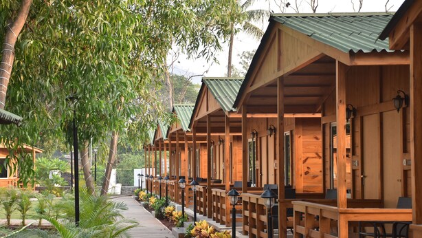 Wooden cabins with a covered porch and outdoor seating area, surrounded by greenery and trees. - Sai River Resort (Khalapur)