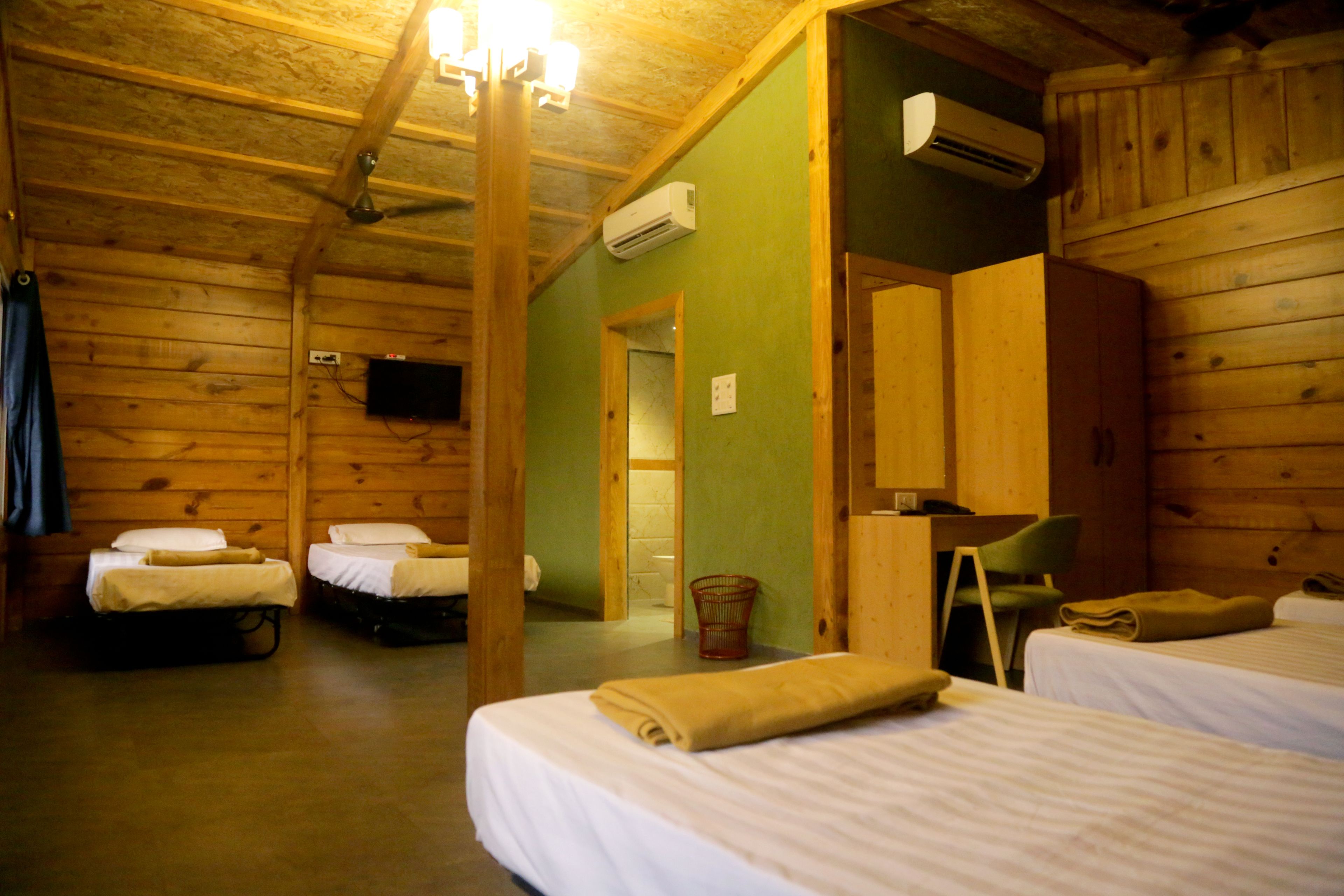 Una habitación tipo cabaña con dos camas, techo de madera, aire acondicionado y televisor en la pared.