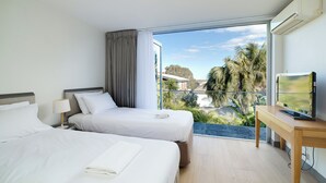 Een hotelkamer met twee bedden, een televisie en een balkon met uitzicht op palmbomen en gebouwen.