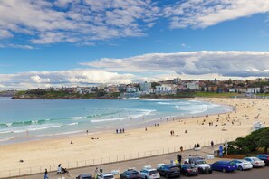 A beach with people, cars, and buildings in the background.