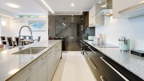 Een moderne keuken met een groot eiland, roestvrijstalen apparatuur en uitzicht op de eetruimte.