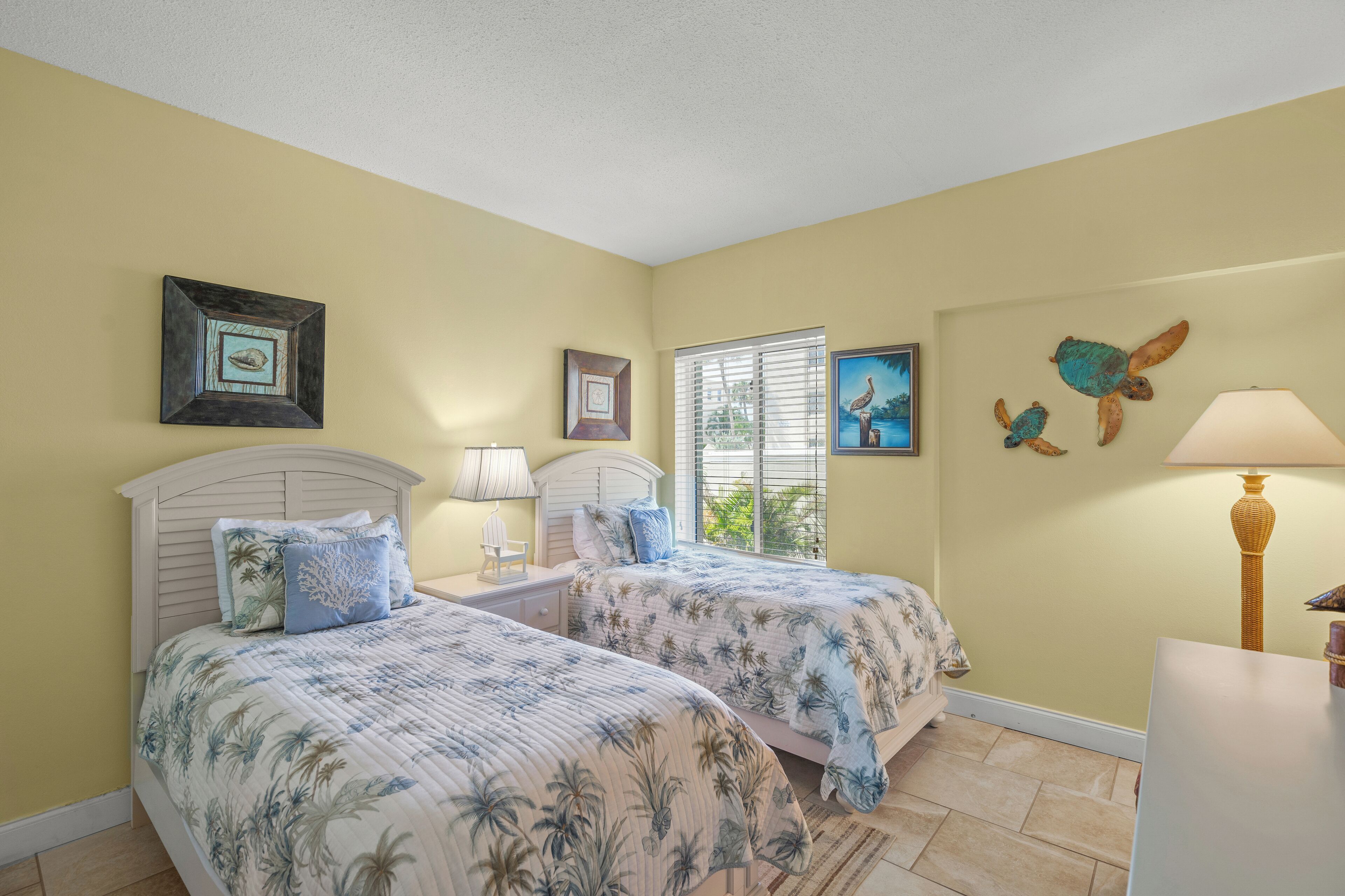 A bedroom with two beds, a window with blinds, and wall art.