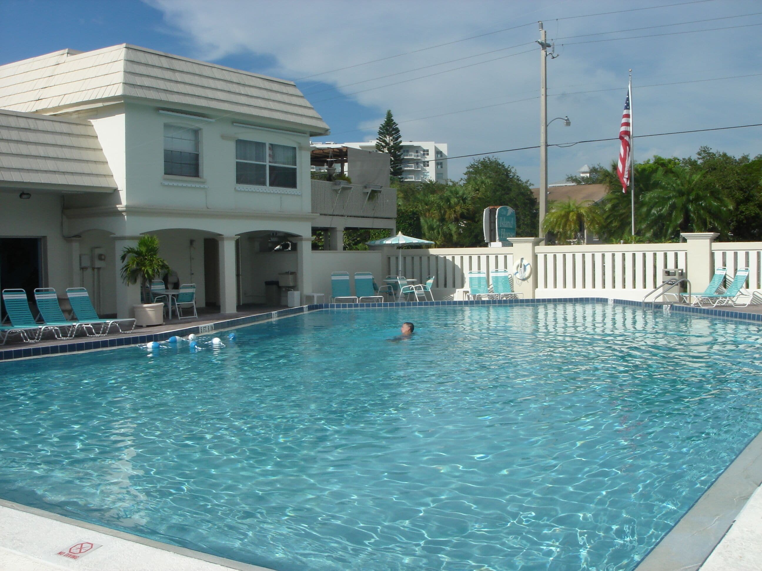 A swimming pool with lounge chairs and a flagpole with an American flag.