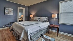 Een slaapkamer met een bed, nachtlampen, een nachtkastje, een spiegel en een raam met zonwering.