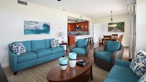 A living room with a sofa, armchairs, and a coffee table. There is a kitchen in the background.