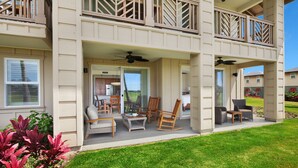 A two-story residential building with a covered patio area featuring outdoor furniture, a dining set, and a kitchen visible through an open door.
