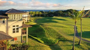 A golf course with a clubhouse, palm trees, and a view of the ocean.
