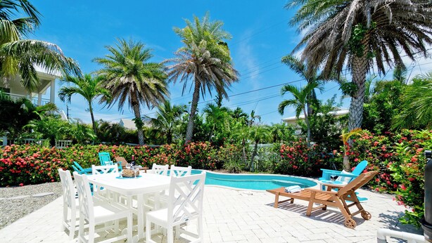 A pool area with white outdoor furniture, surrounded by lush greenery and palm trees. - Poolside Relaxation Just Steps from the Gulf (Anna Maria)