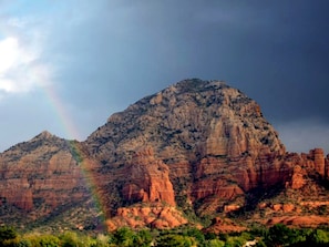 A mountain with a rainbow, surrounded by red rock formations.