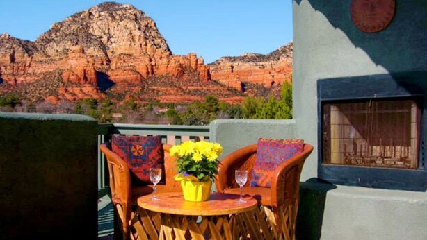 Eine Terrasse mit Korbmöbeln, einem Tisch mit einer Vase gelber Blumen und Blick auf rote Felsformationen.