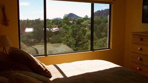 Ein Schlafzimmer mit einem großen Fenster, das einen Blick auf eine gebirgige Landschaft und ein Haus bietet.
