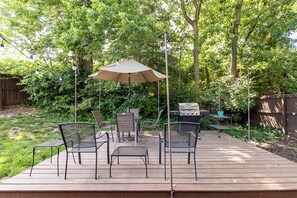 Une terrasse dotée de mobilier d’extérieur, d’un barbecue et d’une pergola illuminée de guirlandes lumineuses.