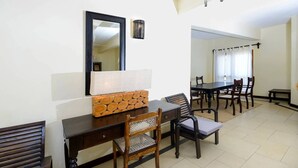 Un espace repas comprenant une longue table, des chaises, un buffet en bois, un miroir et un luminaire suspendu.