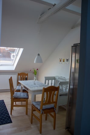 Un espace repas comprenant une table, des chaises, un vase de fleurs, un luminaire suspendu et une vue à travers une lucarne.