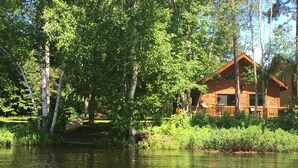 A cabin by a lake surrounded by trees. - Cabin on AuTrain River a few blocks from Lk Superior, 10 mi from Munising (Au Train)