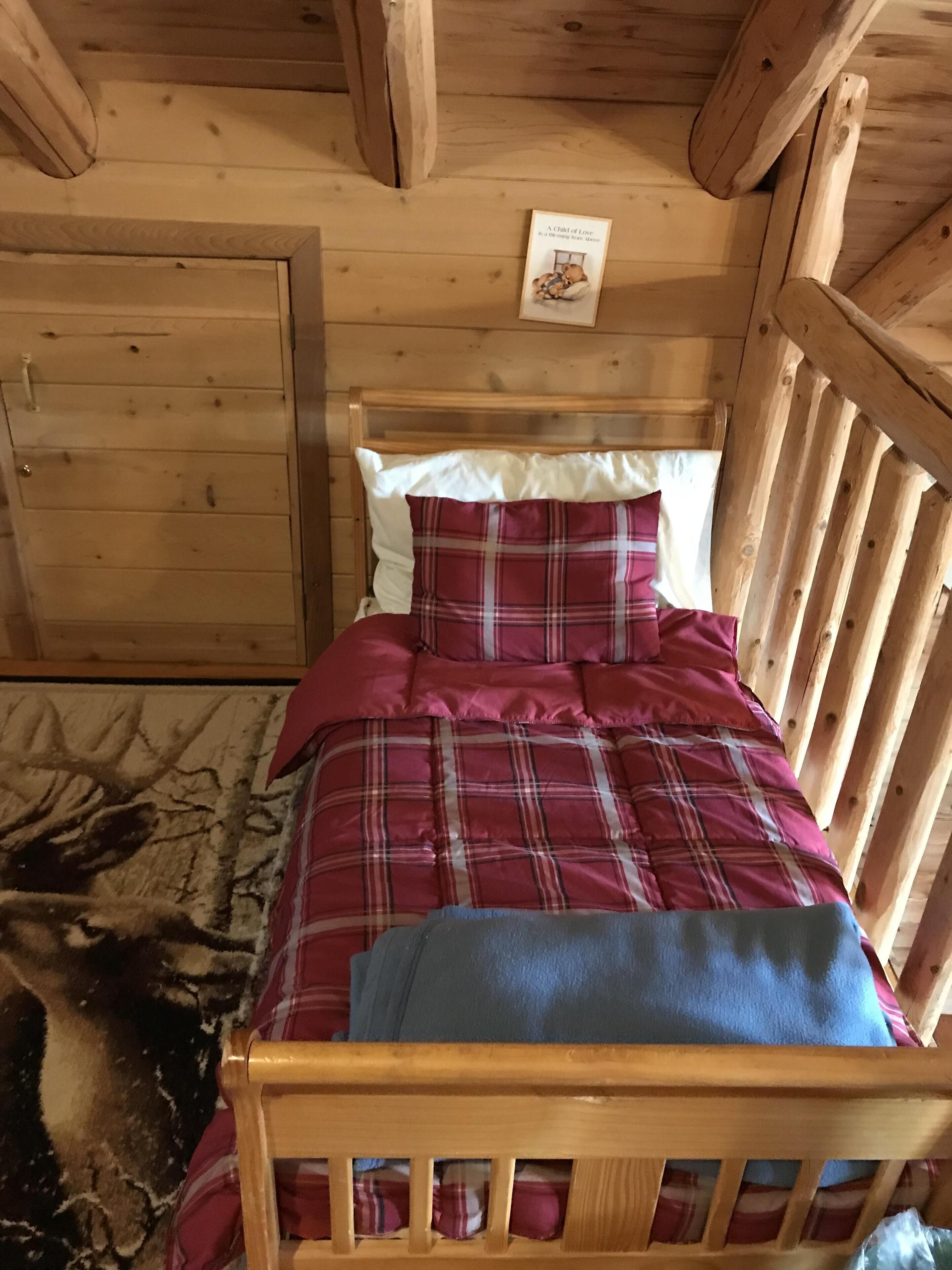 Una cama de madera con colcha y almohadas a cuadros, un cabecero de madera y un cuadro enmarcado en la pared.