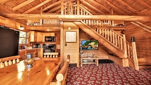A wooden cabin interior with a dining area, kitchen, and a staircase leading to a loft. - Cabin on AuTrain River a few blocks from Lk Superior, 10 mi from Munising (Au Train)