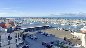 Un port de plaisance où sont amarrés de nombreux bateaux, un parking avec des voitures et un bâtiment sur lequel on peut lire l’inscription « PORT DE PÊCHE ».