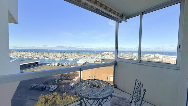 Un balcon avec une table et des chaises, offrant une vue sur un port de plaisance et sur le paysage urbain.