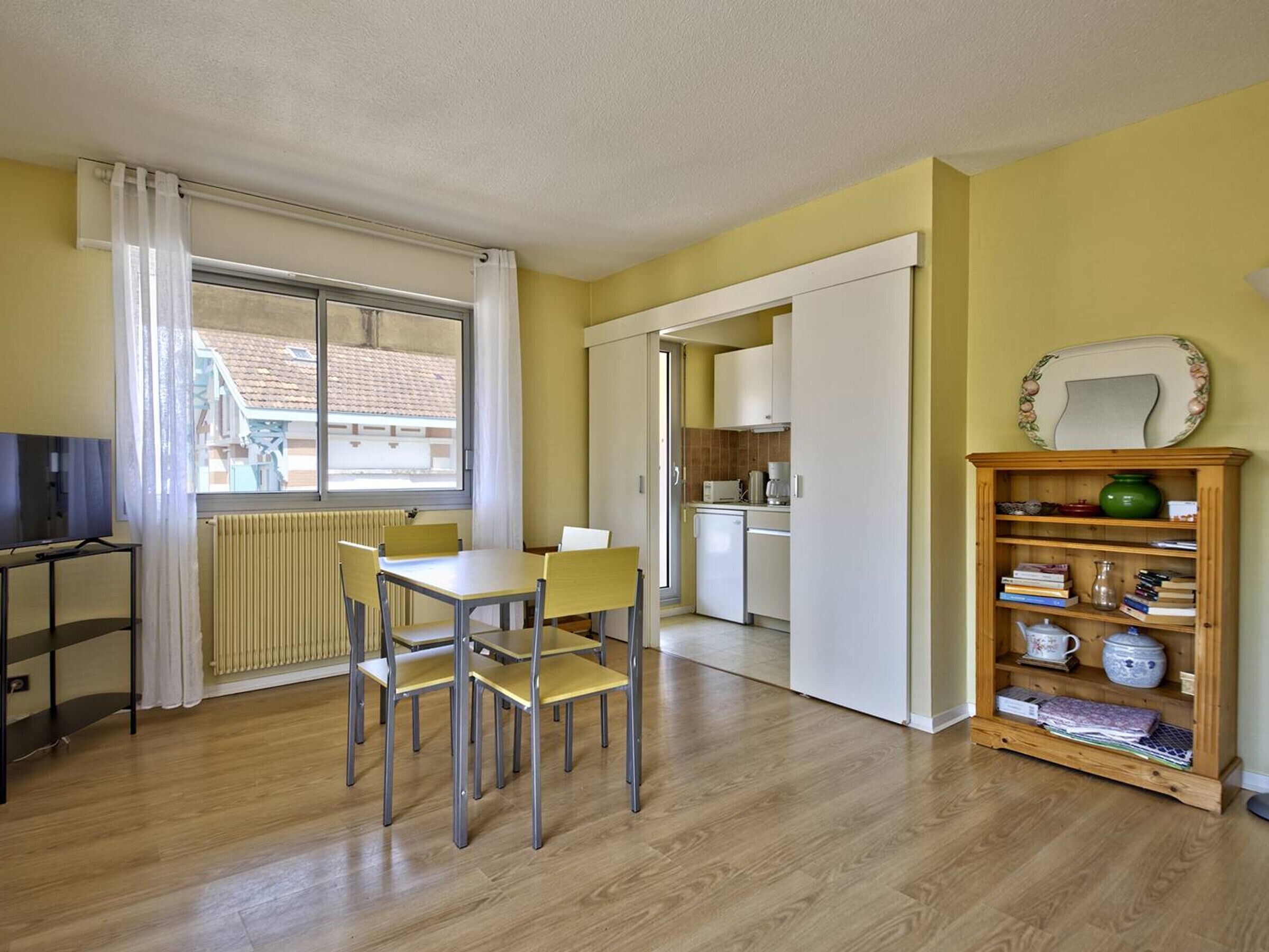 A compact living space with a dining area, kitchenette, and a bookshelf.