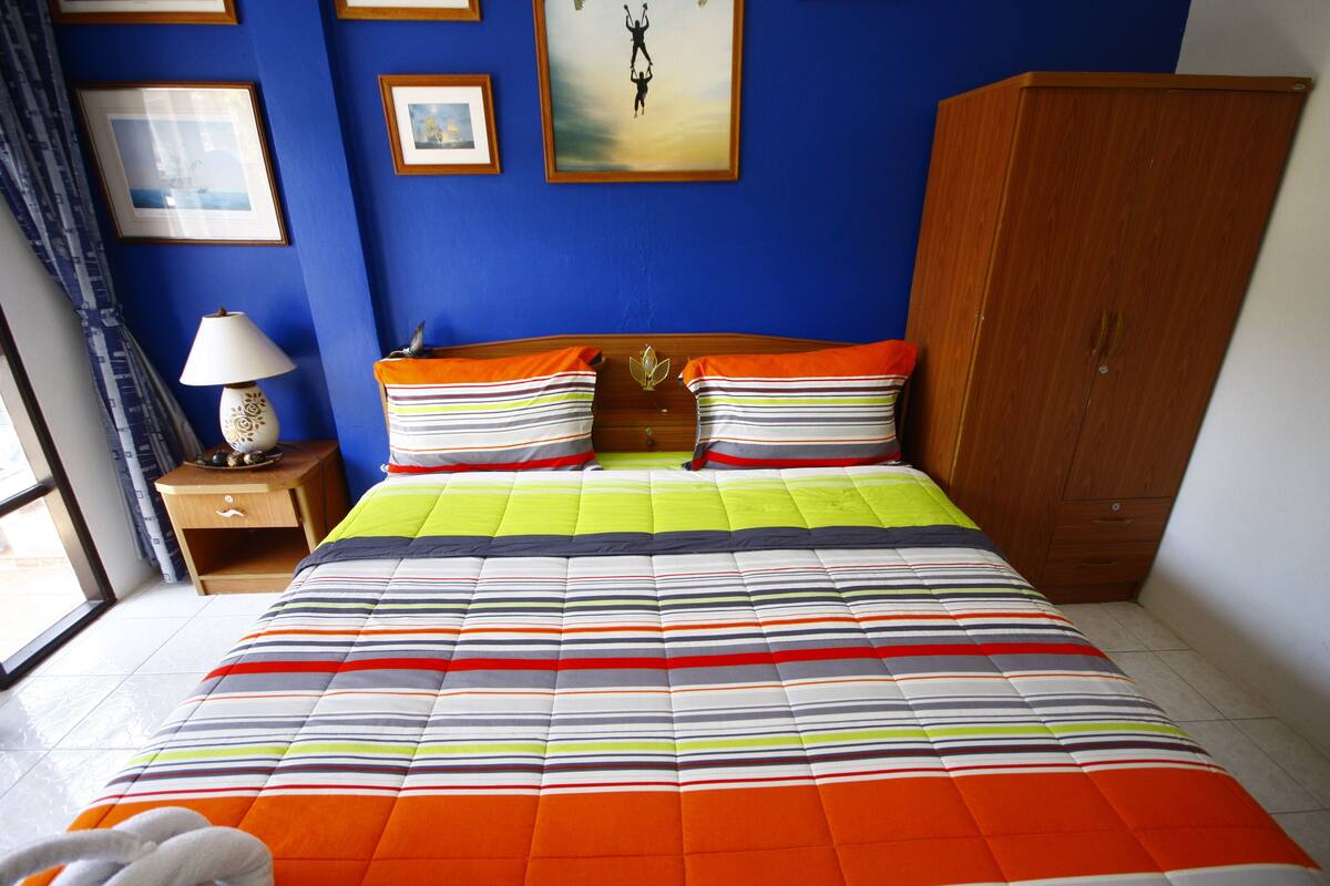 A bed with a striped quilt, a nightstand with a lamp, and a wardrobe.