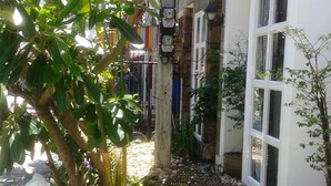 A narrow alley with a small garden area, a white building with multiple windows, and a flag hanging above. - Summer Breeze Inn Hotel (Wichit)