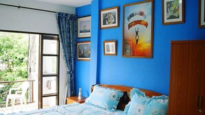A bedroom with a large bed, a wooden wardrobe, and a balcony with a view of greenery. - Summer Breeze Inn Hotel (Wichit)