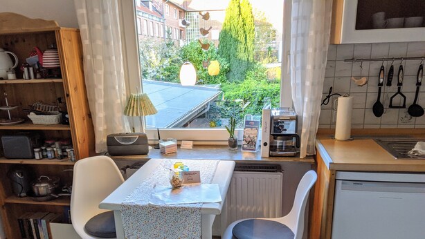 A compact kitchen with a dining table, chairs, a radiator, a Siemens dishwasher, and a view of the garden through a window. - Cozy inner city apartment: City escape Lüneburg (Lüneburg)