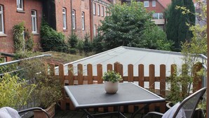 A patio with a table and chairs, surrounded by a wooden fence and greenery. - Cozy inner city apartment: City escape Lüneburg (Lüneburg)