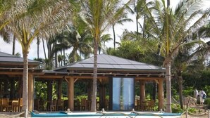 A beachside building with a covered seating area, a pool, and two boats.